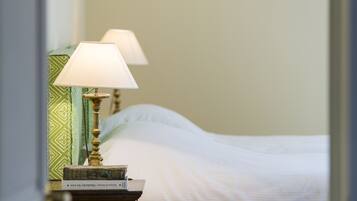 A neatly made bed with white linens, a bedside lamp with a green patterned lampshade, and a book on the nightstand.