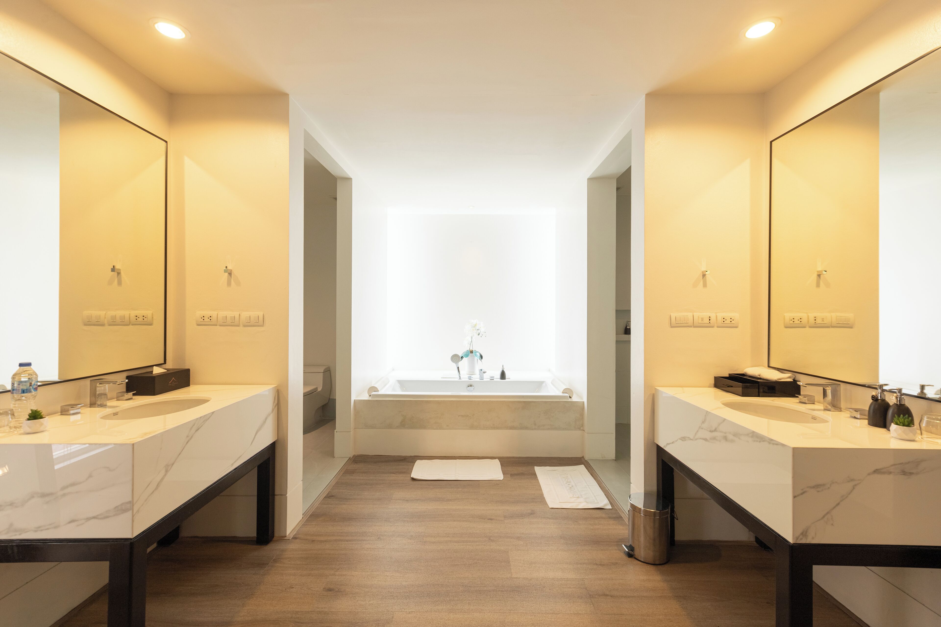 A modern bathroom with two sinks, a large bathtub, and mirrors on both sides.