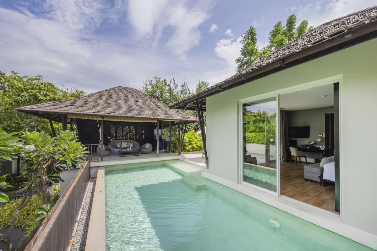 A modern house with a swimming pool, a covered outdoor seating area, and a visible interior with a TV and seating.