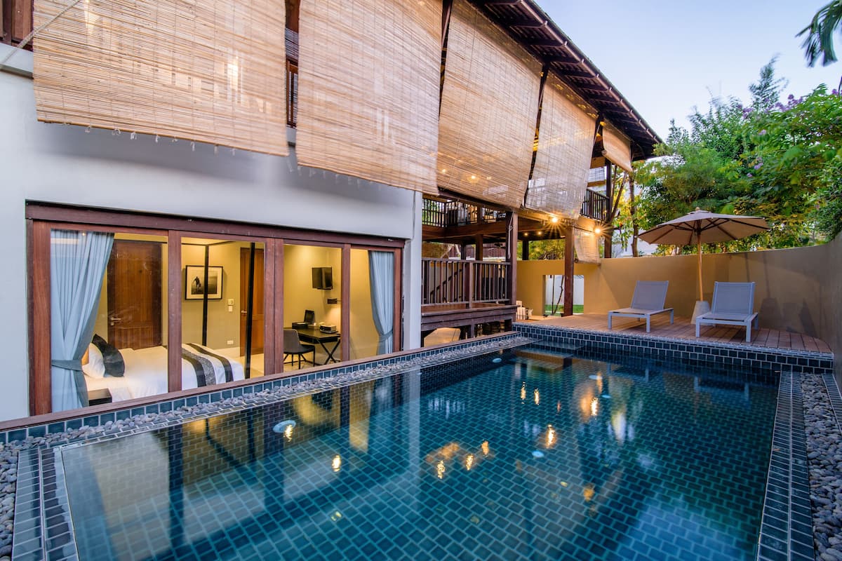 A swimming pool with a tiled edge, a wooden deck, and lounge chairs.