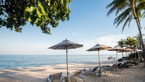 A beach with sun loungers and umbrellas, a palm tree, and the ocean in the background. - The Palayana Hua Hin (Cha-am)