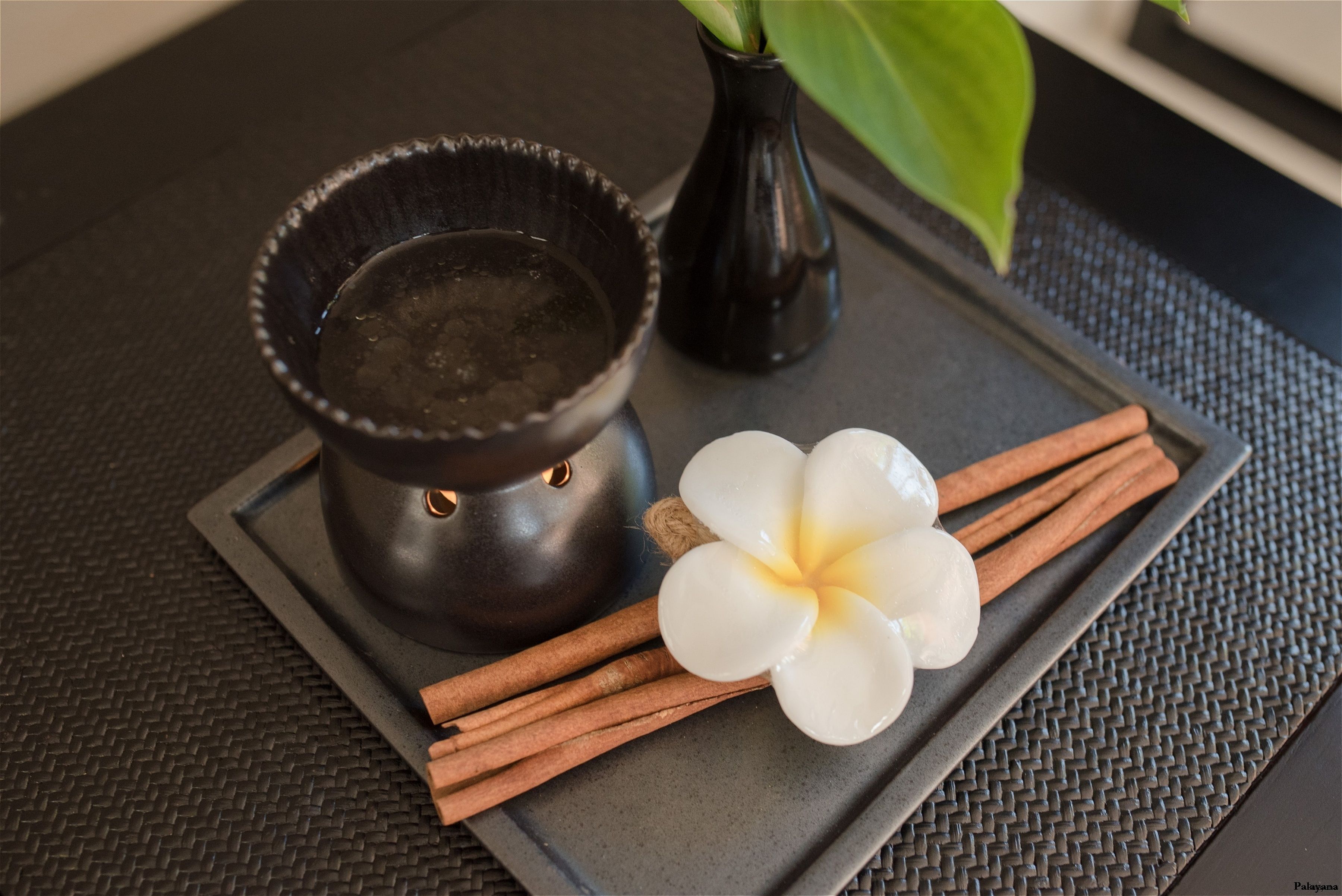 A tray with a candle, a flower, and cinnamon sticks on a textured surface.