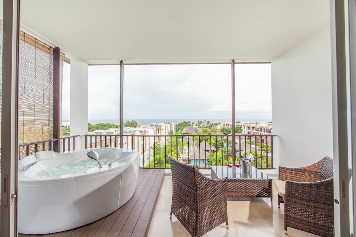 A balcony with a hot tub, wicker furniture, and a view of buildings and the sea.