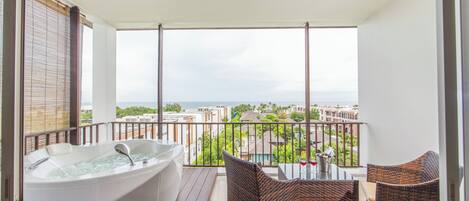 A balcony with a hot tub, wicker furniture, and a view of buildings and the sea.