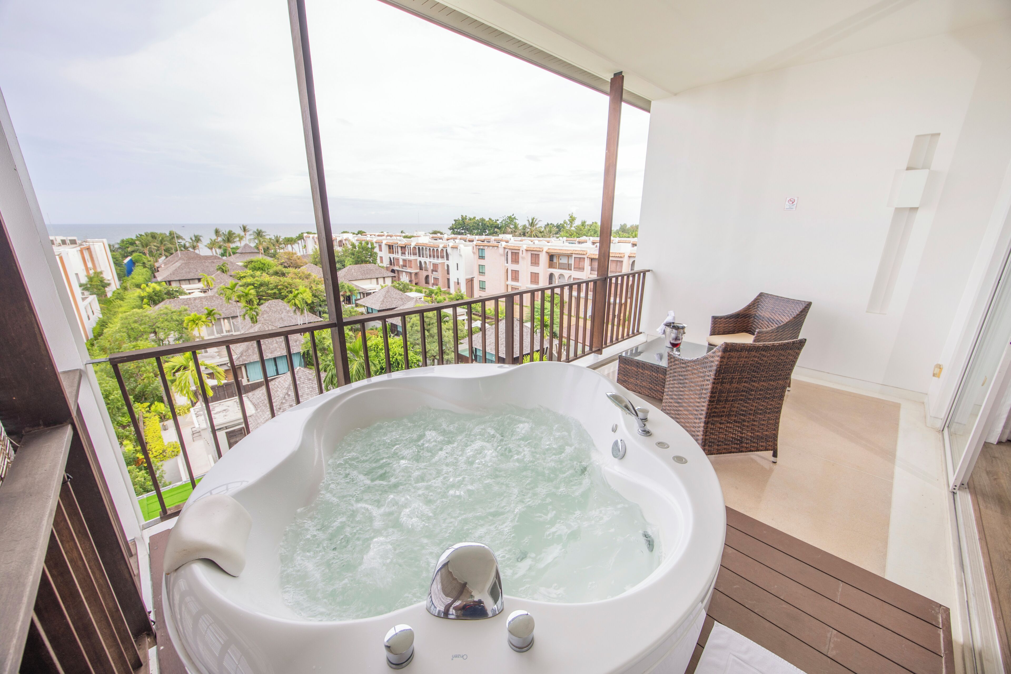 Un balcón con un jacuzzi, muebles de mimbre y vistas a un complejo turístico.