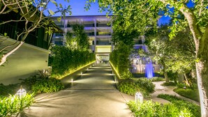 A well-lit pathway leading to a building with a modern architectural design, surrounded by lush greenery and a decorative water feature. - The Palayana Hua Hin (Cha-am)