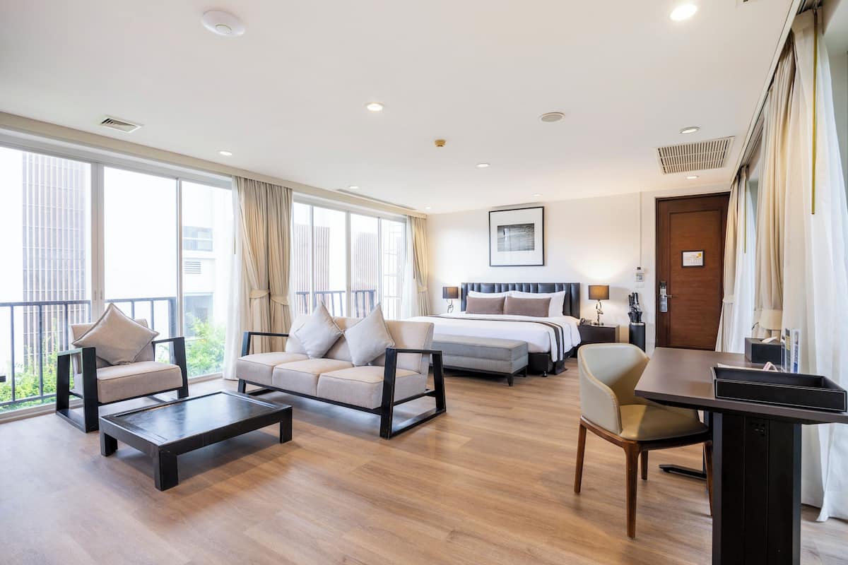 A hotel room with a large bed, a sofa, a coffee table, and a desk.