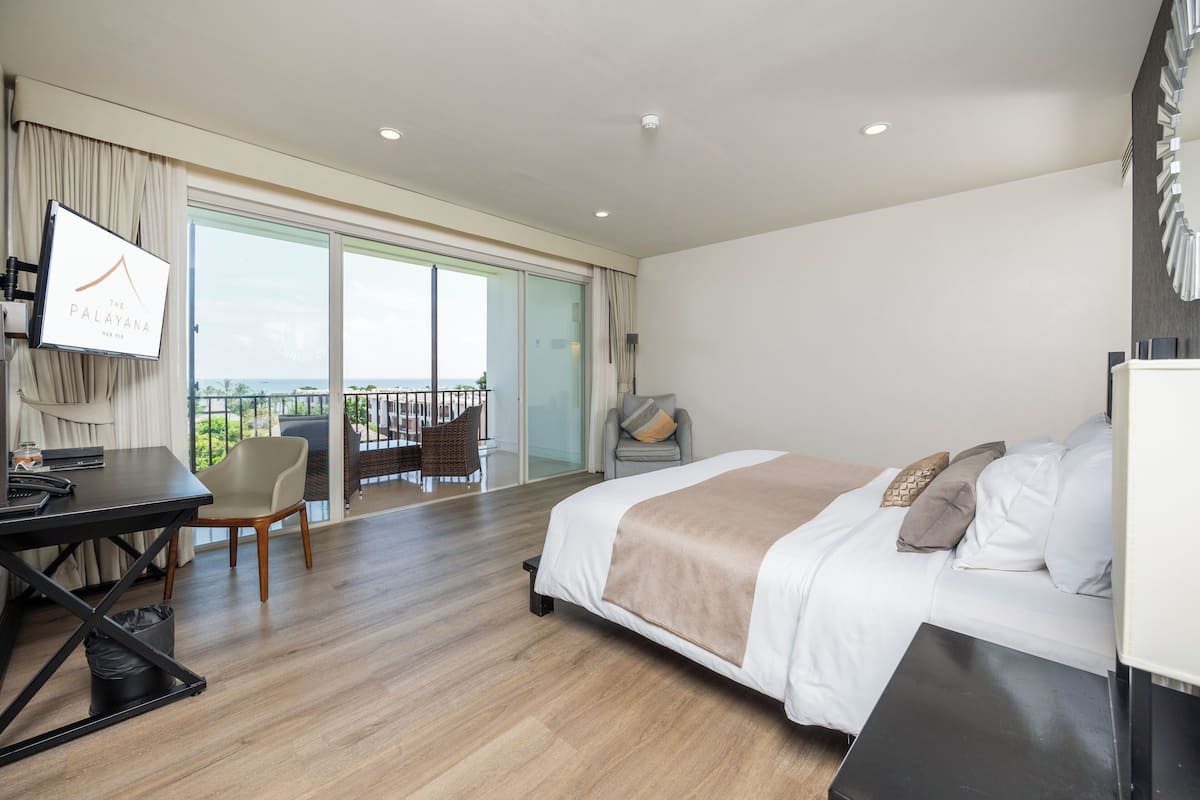 A modern hotel room with a large bed, a desk, and a balcony with a view.