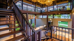 A multi-level wooden interior with a staircase, wicker ceiling chandeliers, and a balcony with a view of greenery. - The Palayana Hua Hin (Cha-am)