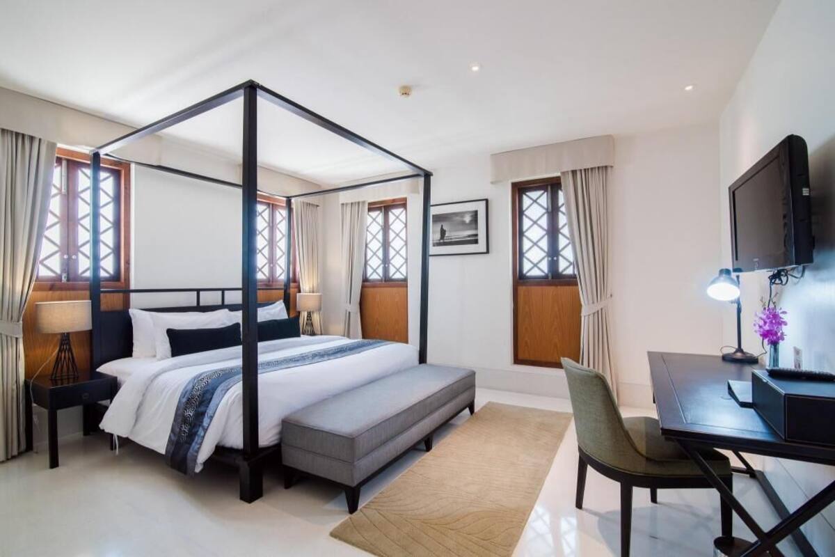 Uma cama com dossel, uma escrivaninha, uma cadeira, uma televisão e uma janela com cortinas.