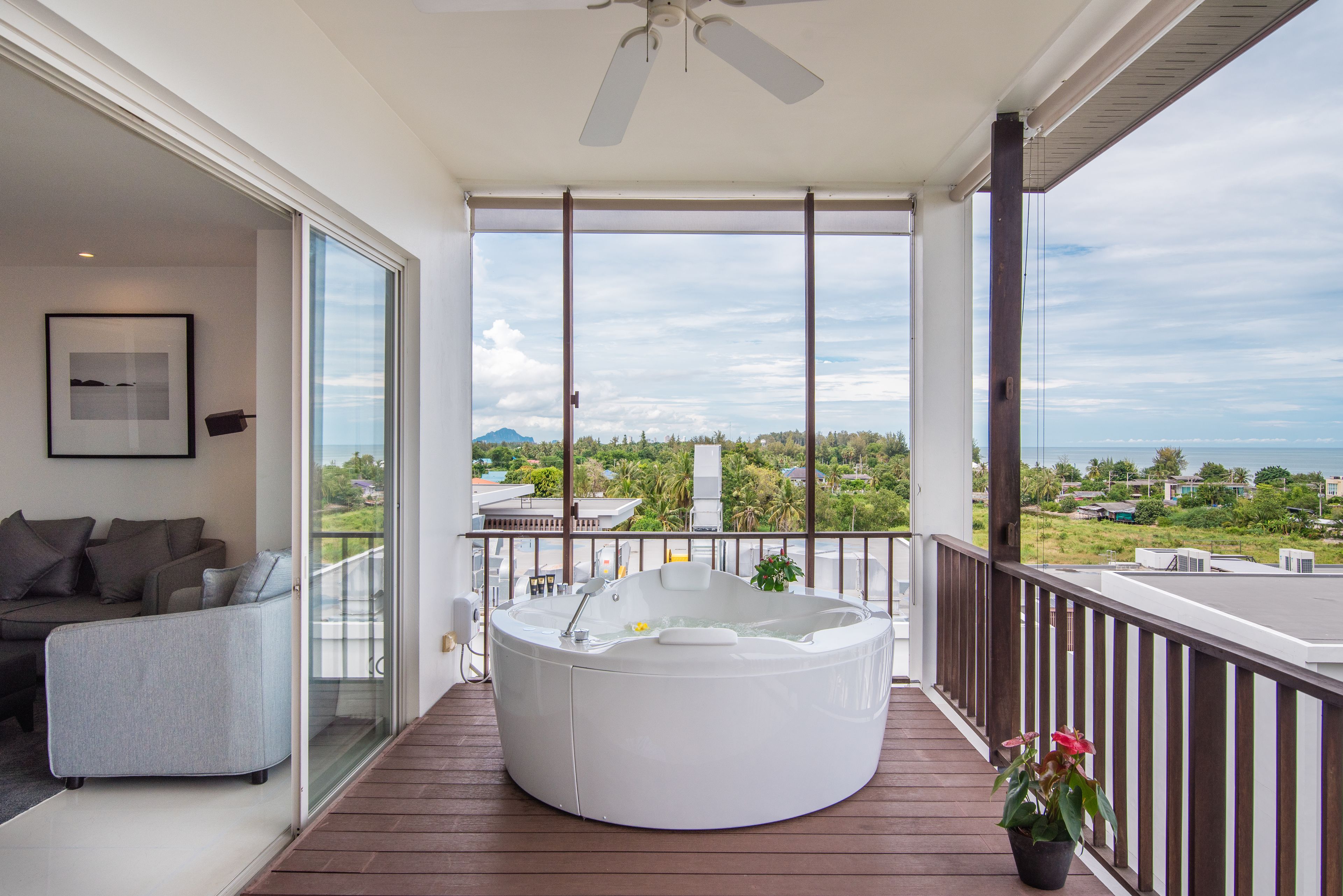 A balcony with a hot tub, a sofa, and a view of the ocean and greenery.