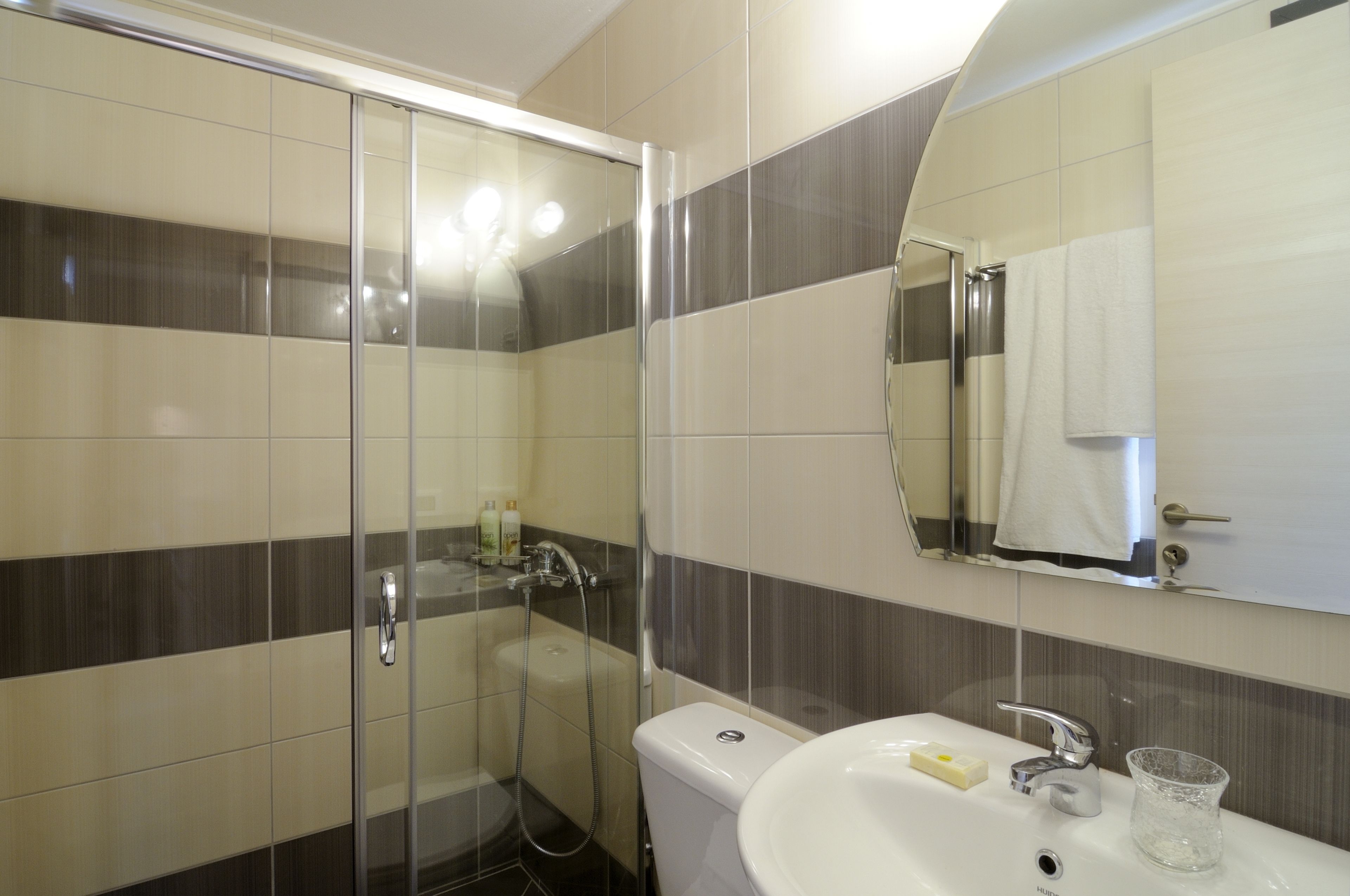 A modern bathroom with a glass shower enclosure, a toilet, a sink with a mirror, and a towel hanging on the wall.