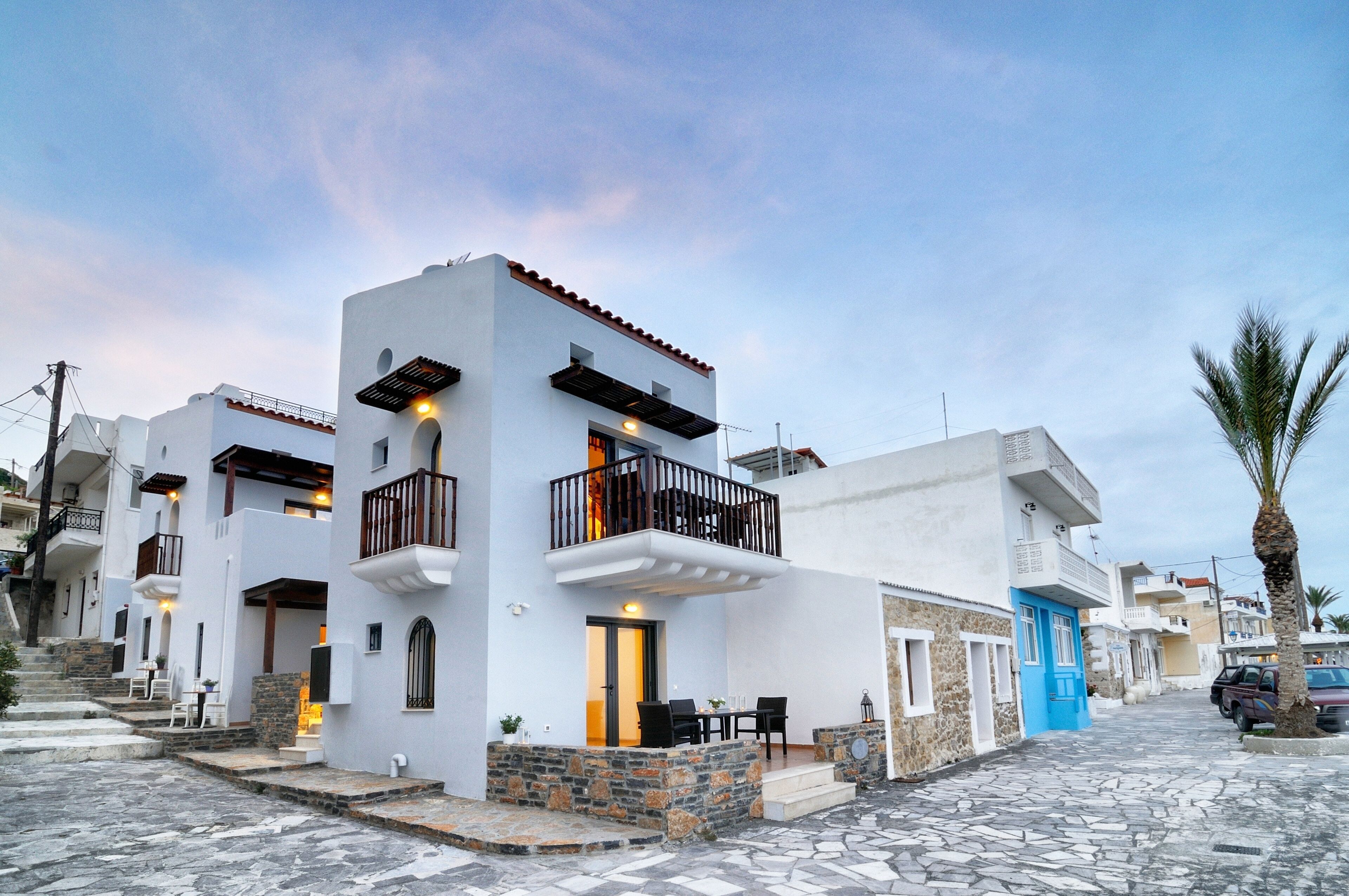 A white building with a balcony, stone steps, and a blue door.