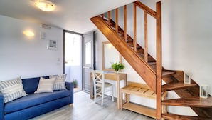 A modern living room with a blue sofa, wooden staircase, and a desk with a plant. - Myrtos Mare Suites (Ierapetra)