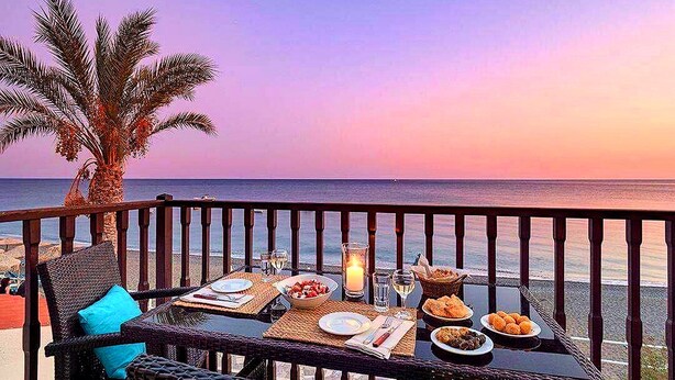 A dining table set with plates, glasses, and a candle on a balcony overlooking the sea. - Myrtos Mare Suites (Ierapetra)