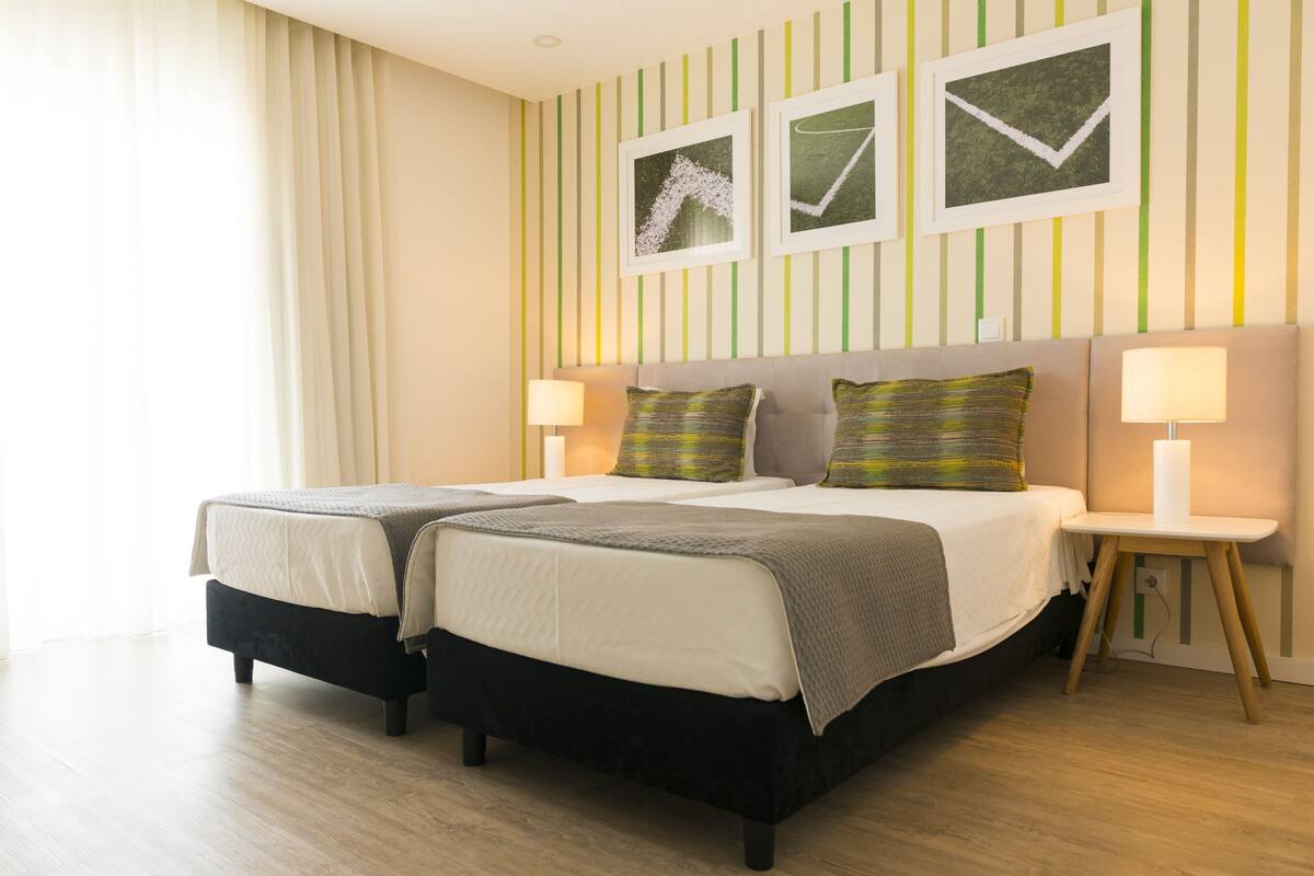 A double bed with two pillows, a bedside table with a lamp, and a wall with striped wallpaper and framed pictures.