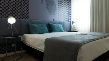 A modern bedroom with a grey sofa bed, teal pillows, a white duvet, and a patterned wall.