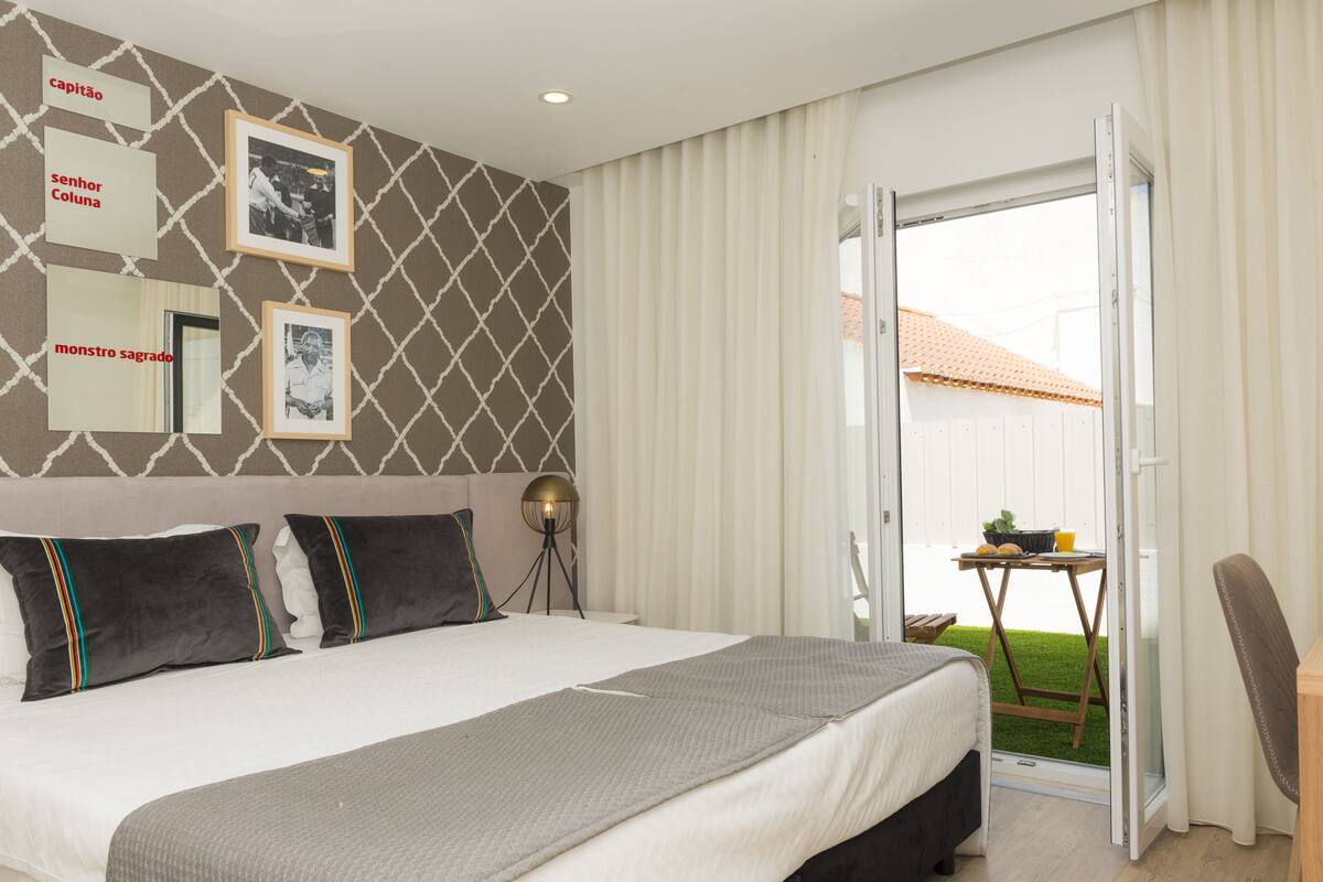 A hotel room with a bed, a bedside table, a lamp, and a view of the outdoors through a sliding door.