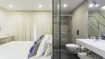 Un baño moderno con ducha envuelta en vidrio, inodoro blanco y lavabo blanco con espejo.