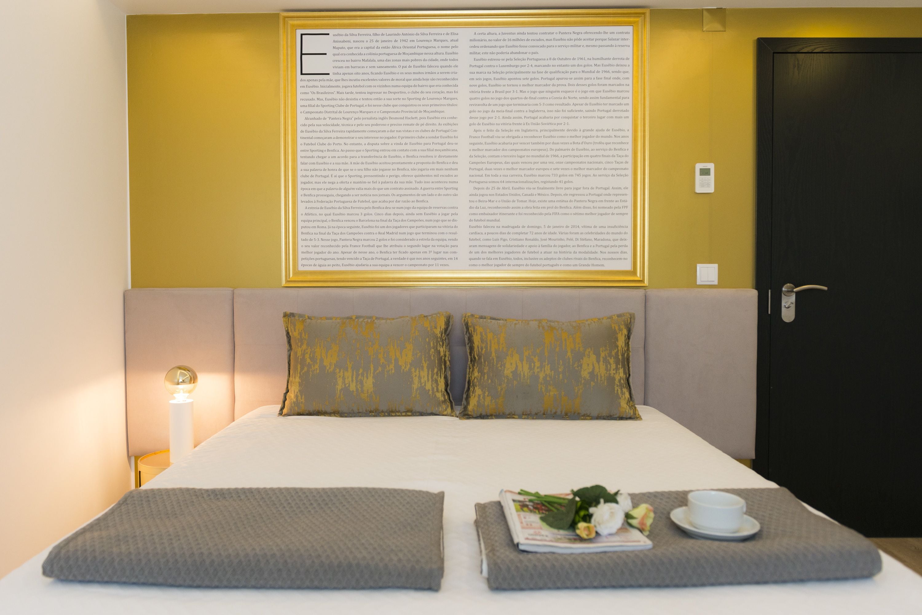 Un lit bien fait, avec deux oreillers, une lampe de chevet et un document encadré accroché au mur.