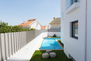 Una zona residencial moderna con piscina, césped artificial verde y una valla blanca.