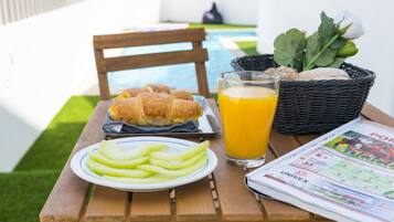 A wooden table with a plate of sliced apples, a basket of bread, a glass of orange juice, and a newspaper.