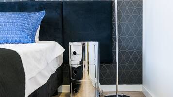 A bed with a white bedspread and a blue pillow, a black headboard, and a metallic trash can with a circular base.
