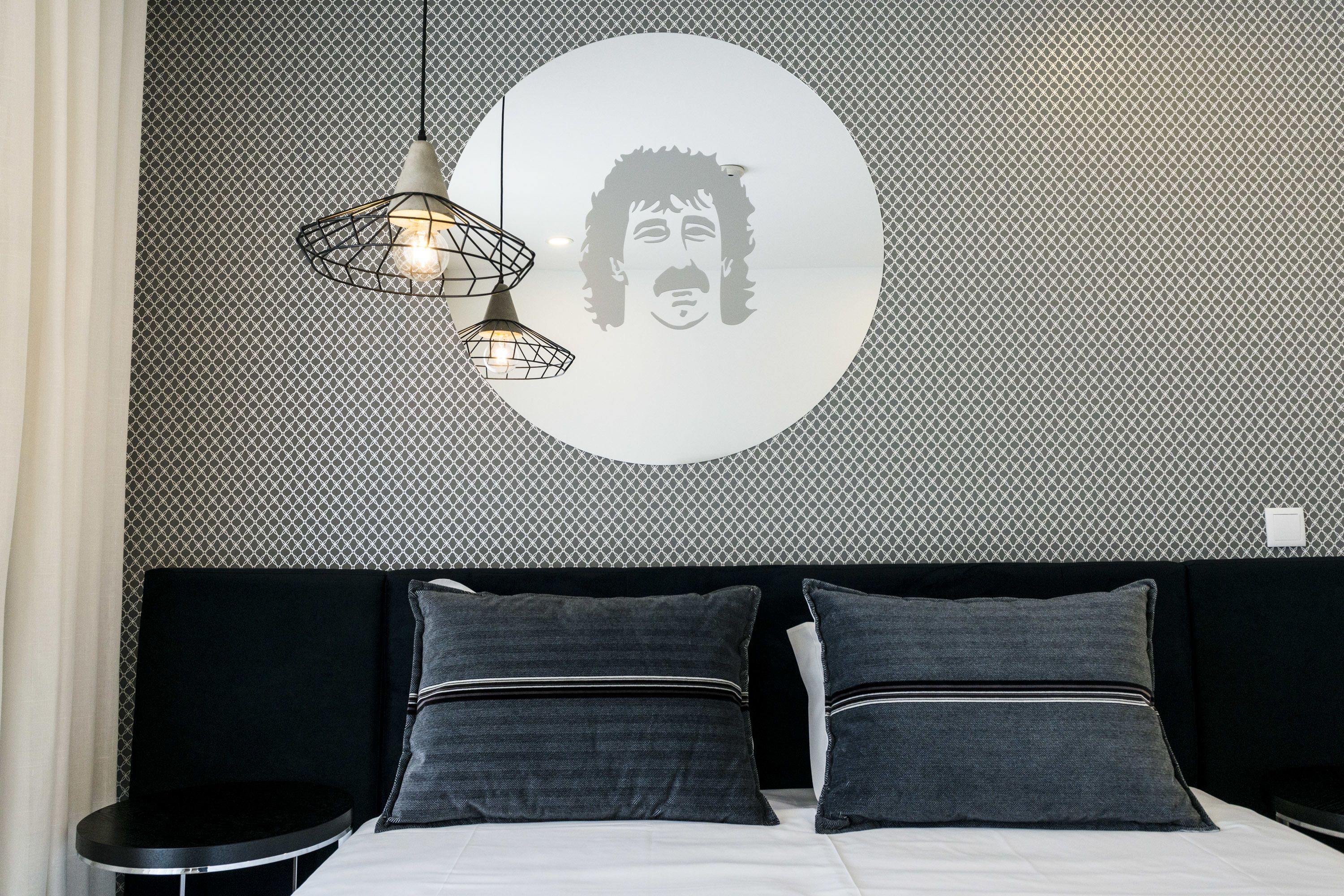 A modern bedroom with a patterned wall, a circular artwork, and a bed with two pillows.
