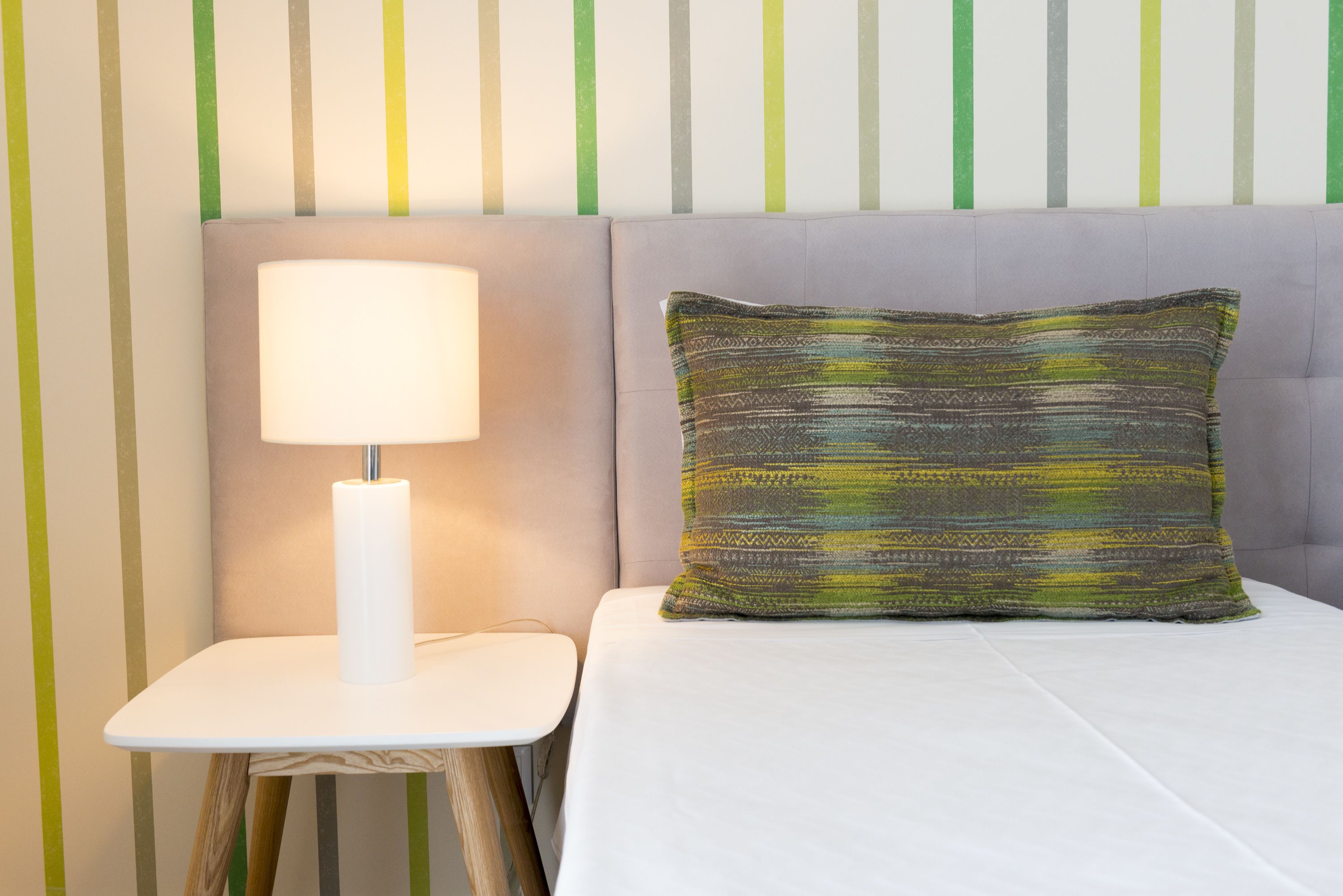 A neatly made bed with a patterned pillow and a bedside lamp on a small table.