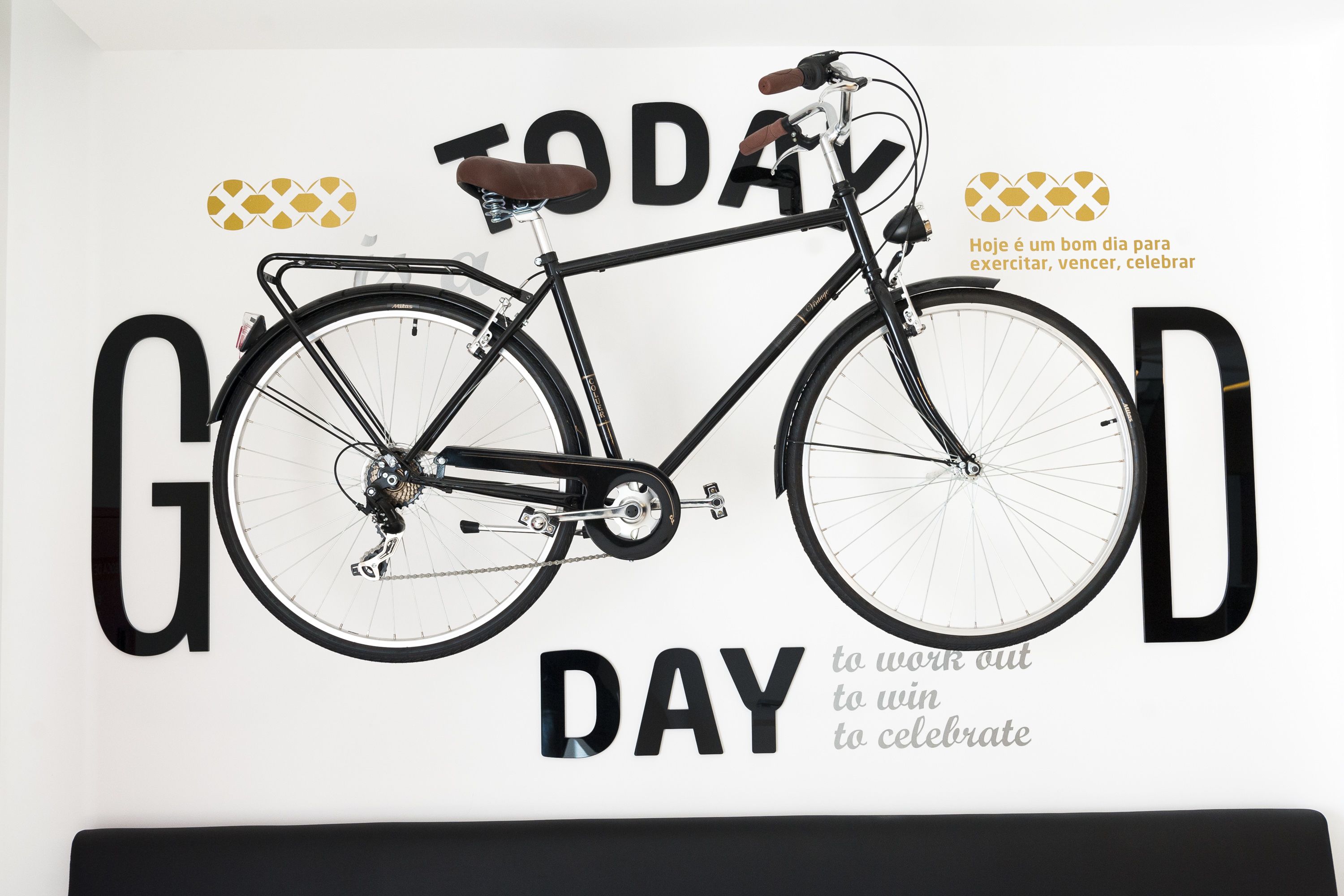 Una pared con una bicicleta negra grande y las palabras "TODAY is a good day to work out, win, celebrate" en blanco y dorado.