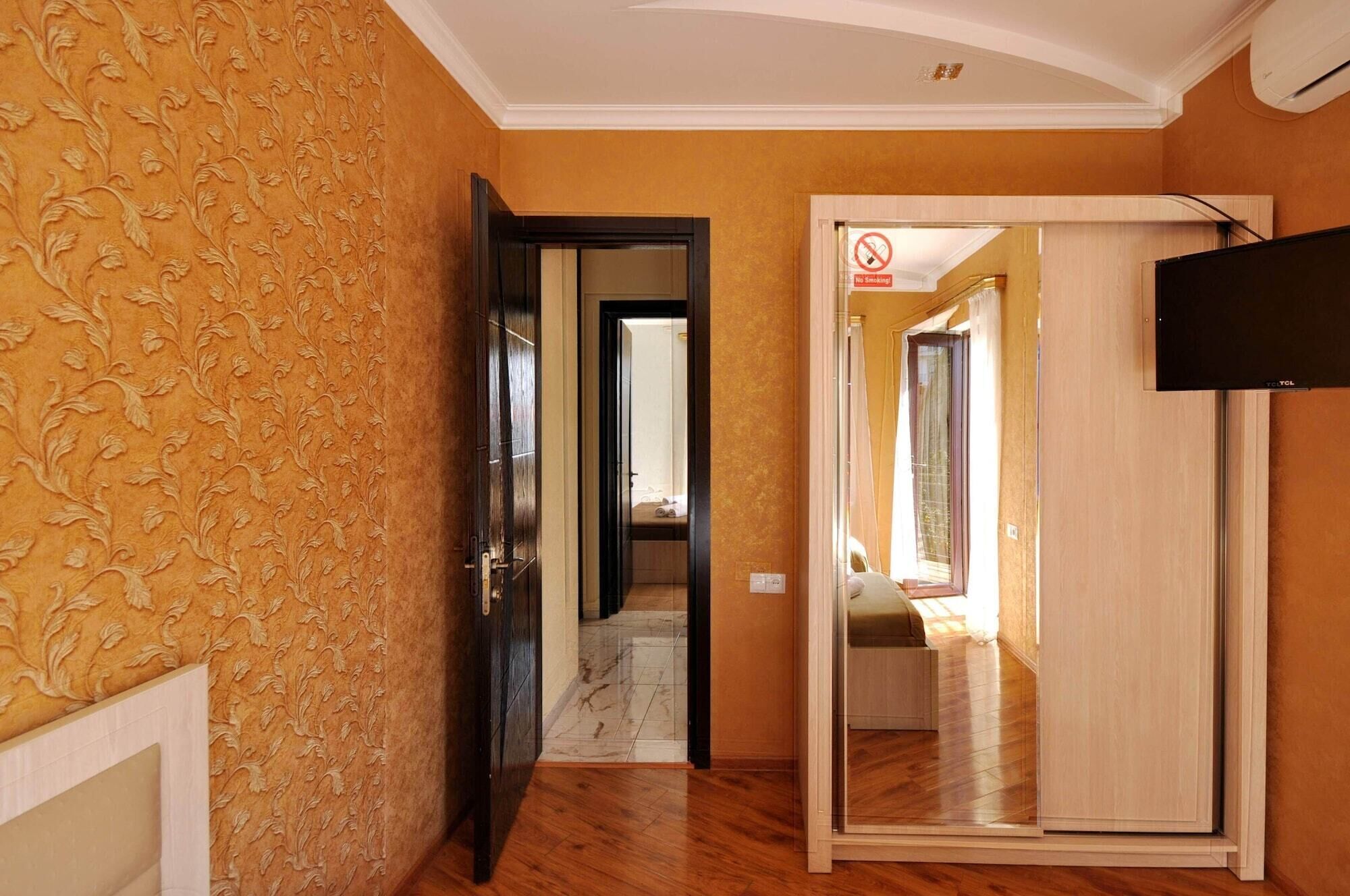 Ein Zimmer mit Holzboden, einer Wand mit Muster und einer Tür, an der ein 'Nichtraucher'-Schild angebracht ist, sowie einem an der Wand montierten Fernseher.