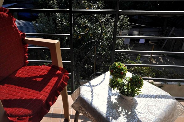A balcony with a chair and a table, a potted plant, and a view of trees and buildings. - Hotel Villa Victoria (Tbilisi)