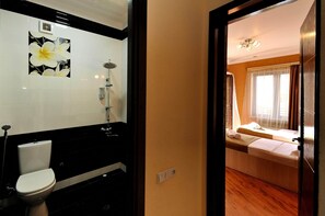 A bathroom with a toilet, a shower, and a sink. The bathroom has a black countertop and white tiles. - Hotel Villa Victoria (Tbilisi)