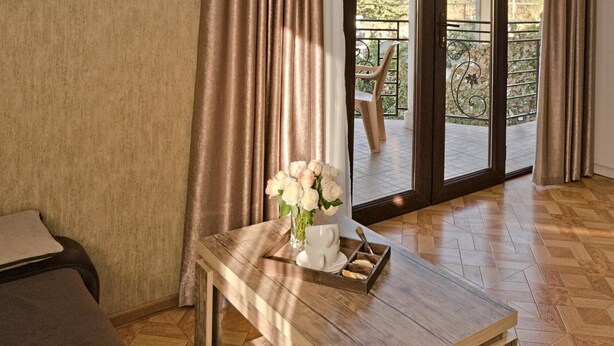 A wooden table with a vase of white flowers and a tray with bread, positioned near a sliding glass door leading to an outdoor area with a chair and a bicycle. - Hotel Villa Victoria (Tbilisi)