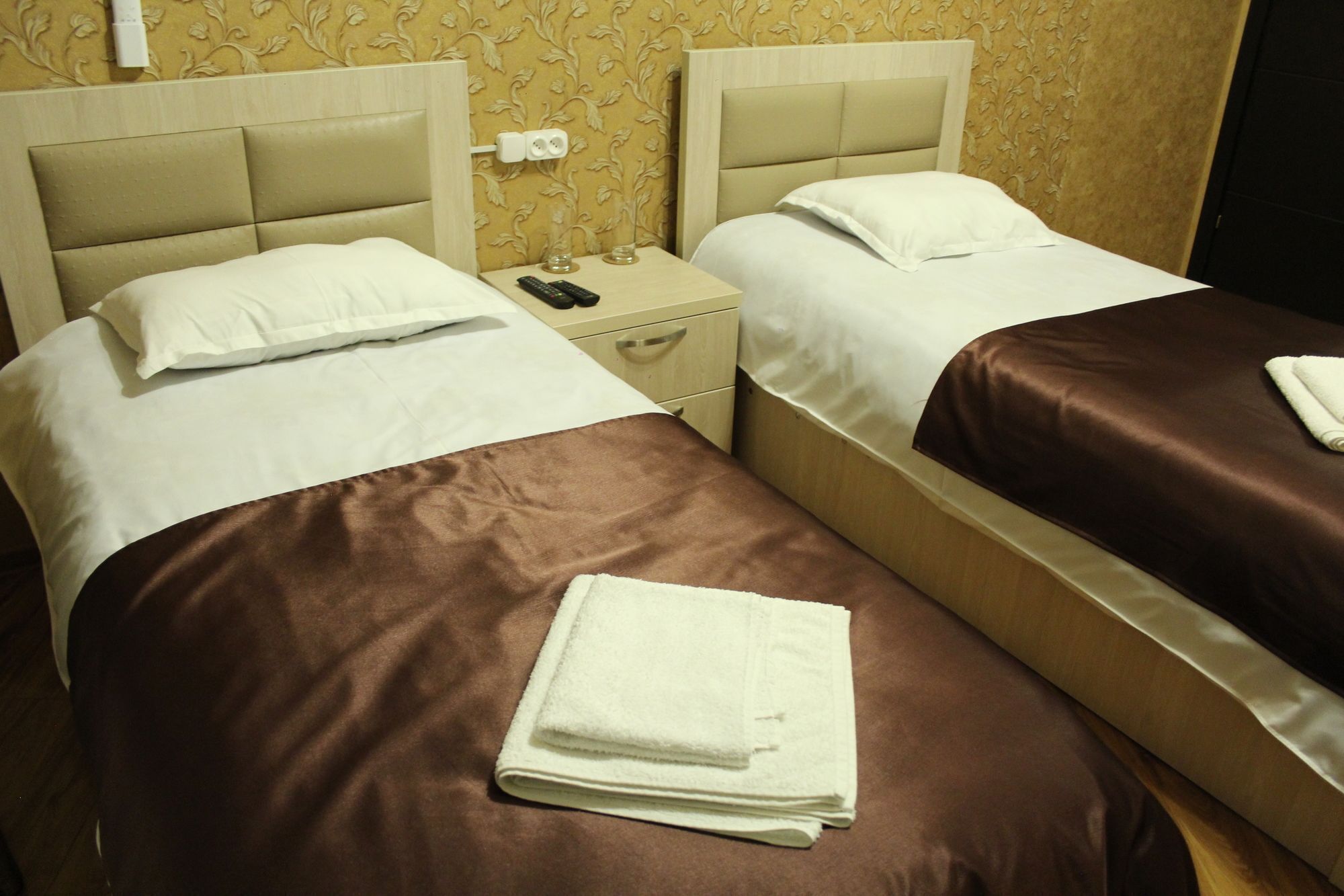 A hotel room with two beds, each with a headboard, a nightstand, and a remote control.