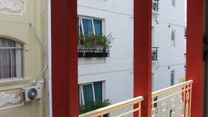 Un balcon avec une balustrade rouge, des plantes en pot et une vue sur les bâtiments voisins.