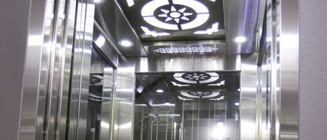 Interior de ascensor con paredes metálicas y techo reflectante.