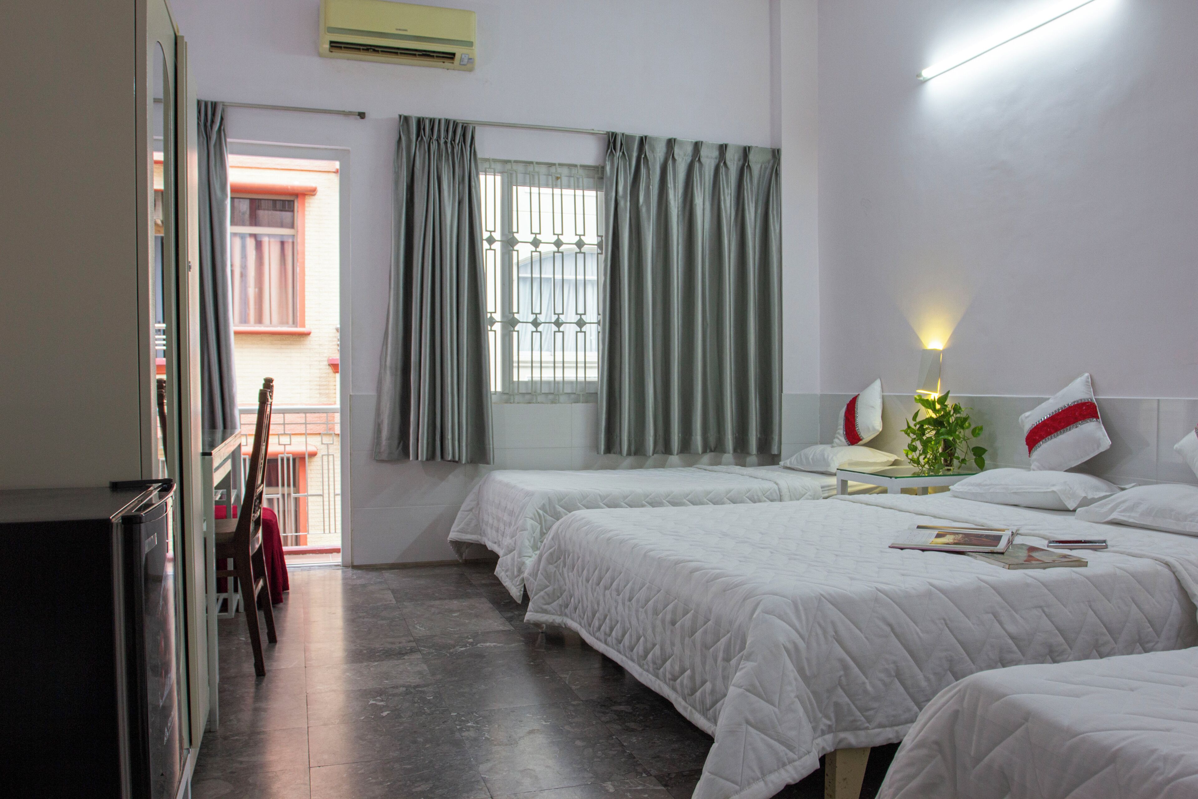 Habitación de hotel con dos camas, una mesita pequeña, una lámpara de noche y una ventana con cortinas.