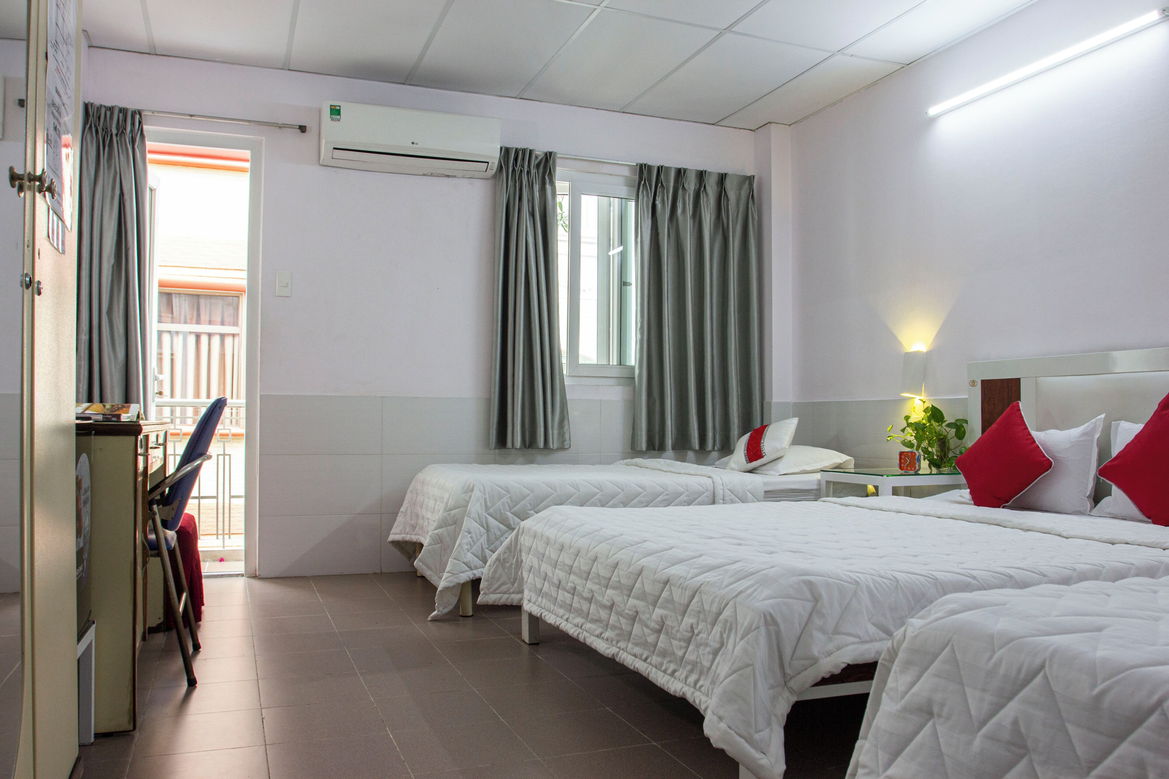 Ett hotellrum med två sängar, ett skrivbord, en stol, en luftkonditionering och ett fönster med gardiner.
