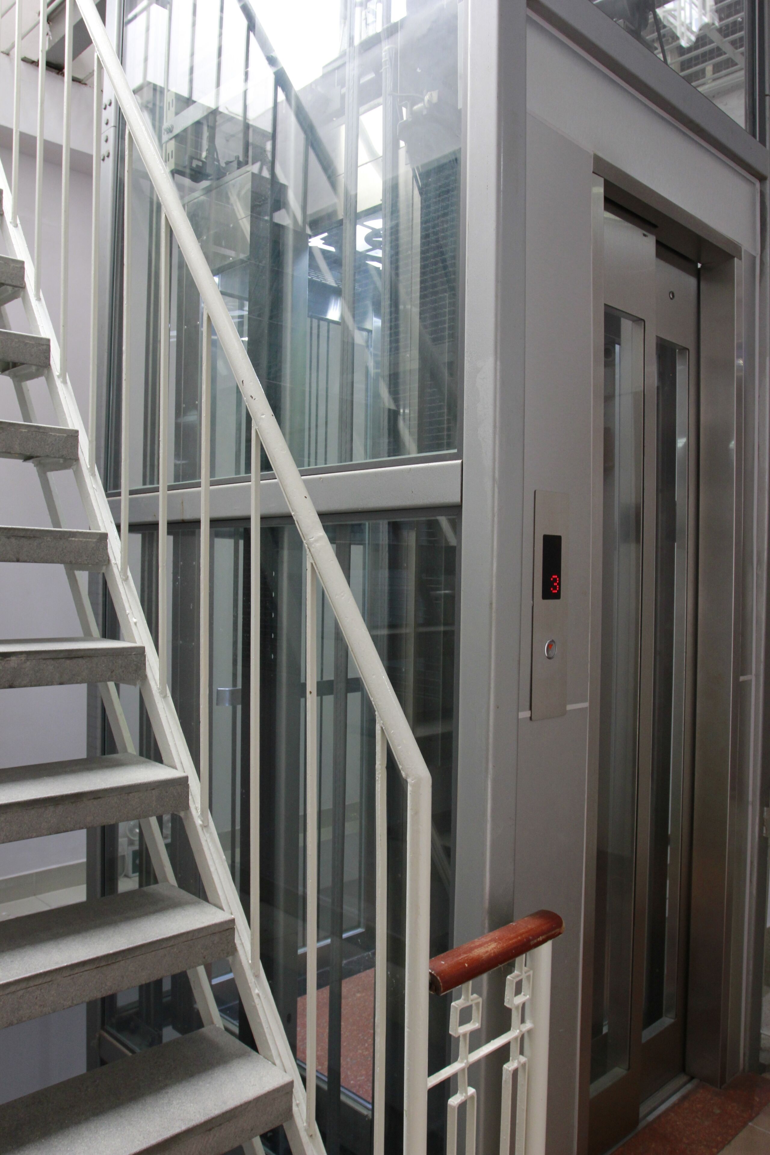 A staircase with a white handrail leading to a glass door with a digital display.