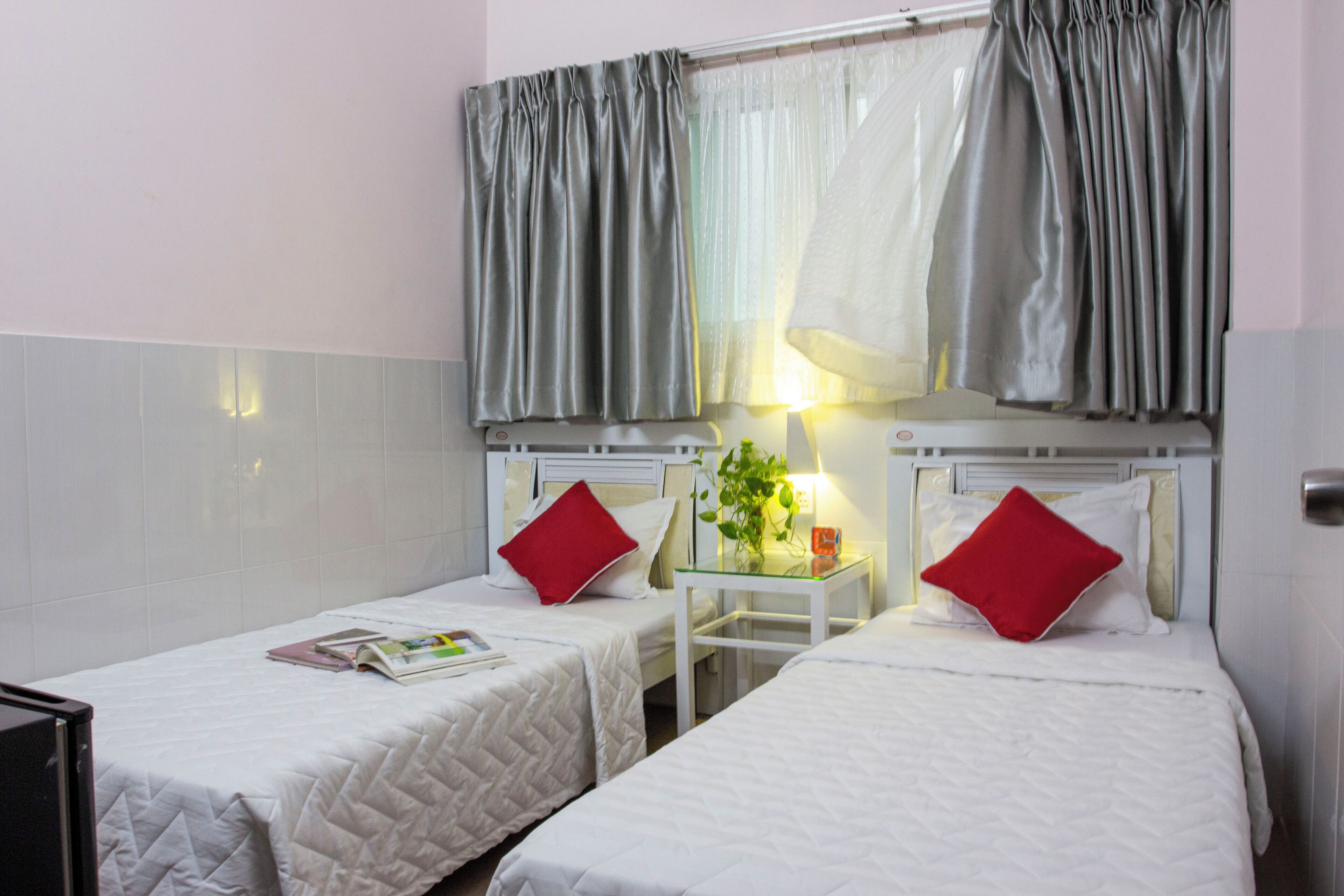 A hotel room with two beds, each with a red pillow, a small table with a plant, and a lamp.