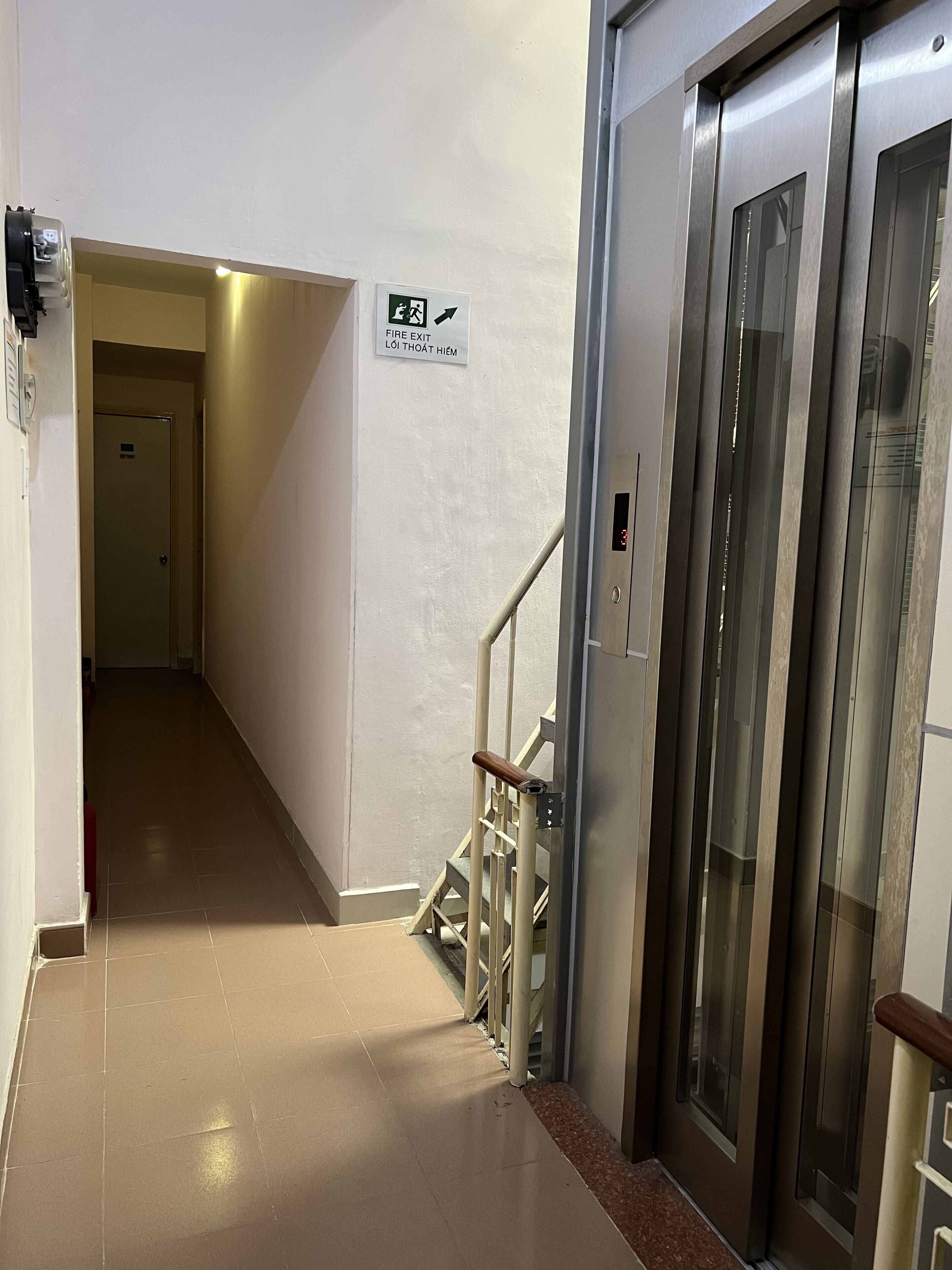 A hallway with a fire exit sign, a staircase, and an elevator.