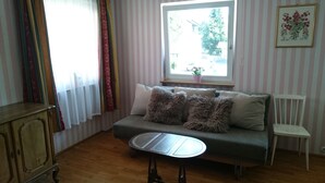 A cozy room with a sofa, a small table, a window with a view of the outdoors, and a wall with a framed botanical illustration.
