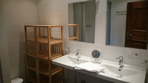 A bathroom with a wooden shelf unit, a sink with a mirror, and a door with a window.