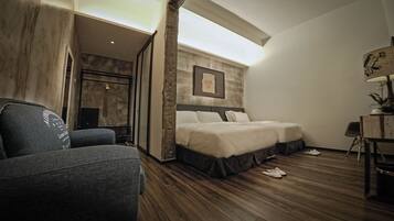 A hotel room with a bed, a chair, a desk with a lamp, and a framed picture on the wall.