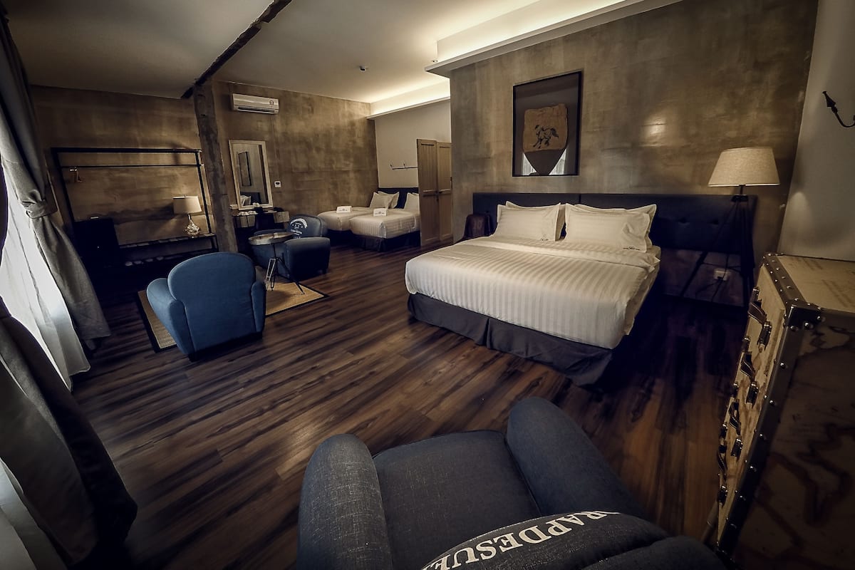 A hotel room with a large bed, a desk with a chair, a sofa, and a wardrobe.