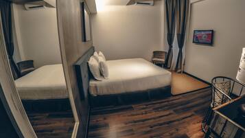 Ein Hotelzimmer mit Holzboden, einem Bett mit weißer Bettwäsche, einem Sessel, einem kleinen Tisch und einer Klimaanlage.
