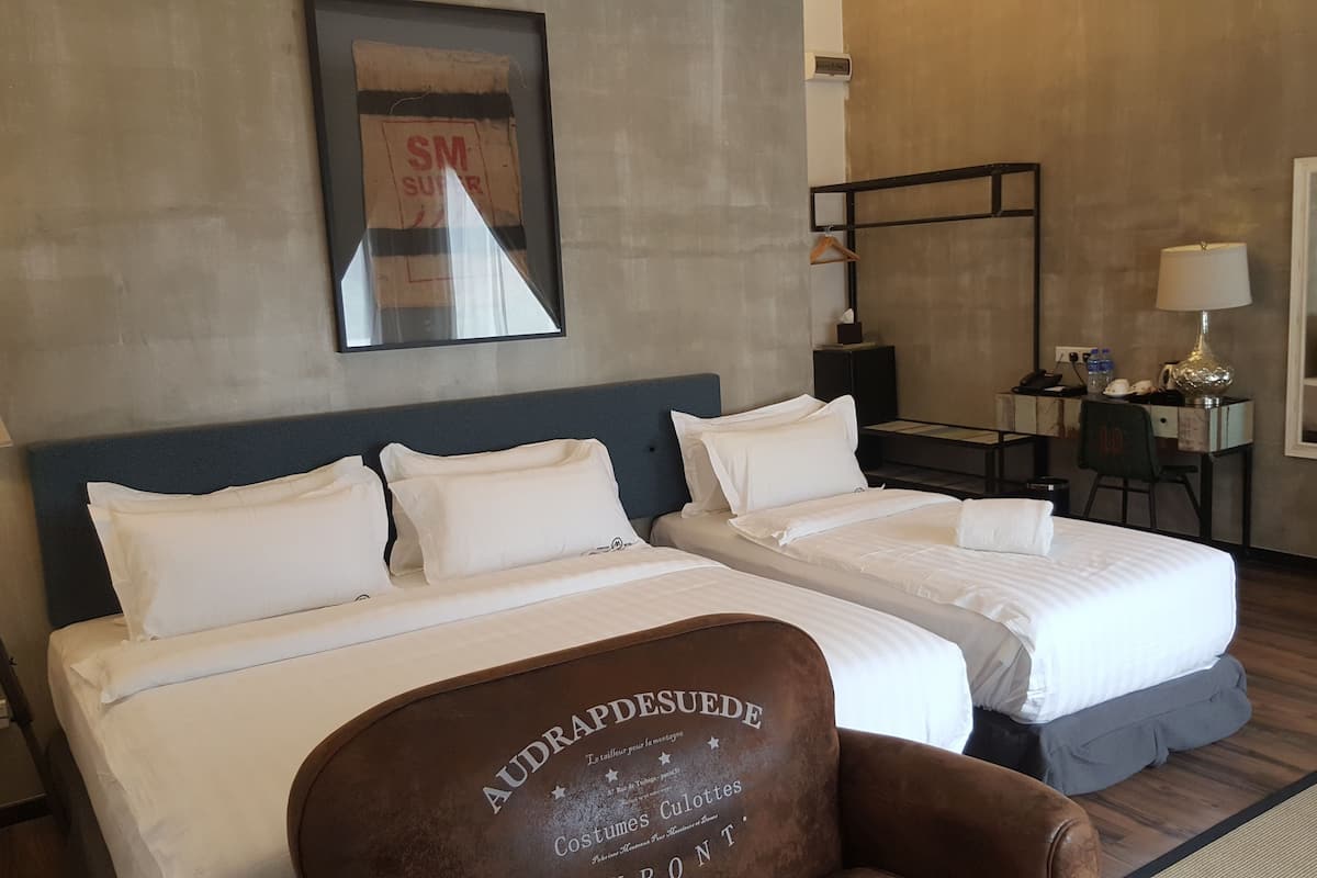 A hotel room with two beds, a desk, a chair, a mirror, and a framed poster on the wall.