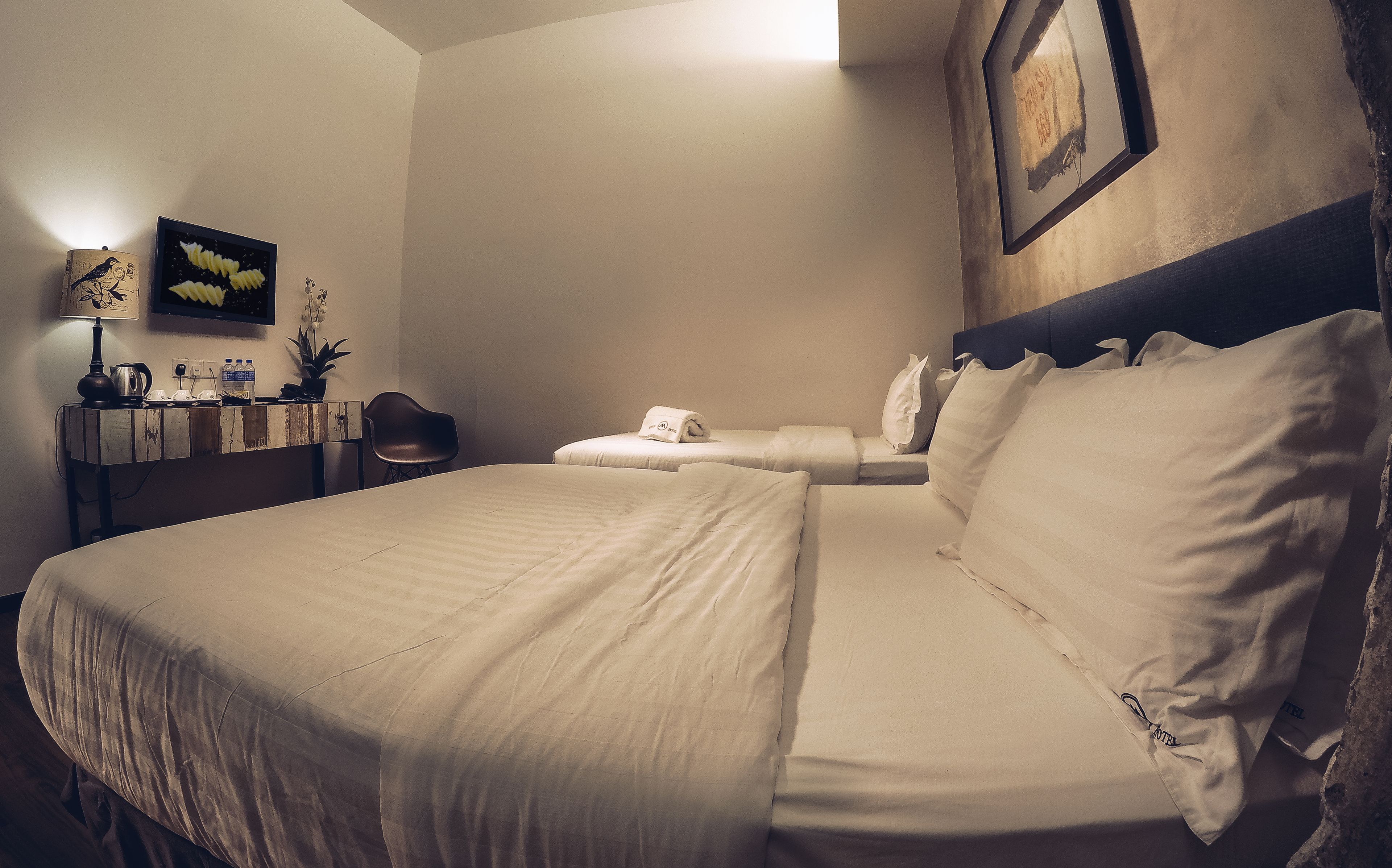 Une chambre d’hôtel avec un grand lit, un bureau avec une lampe, une chaise et une petite table sur laquelle est posée une plante.