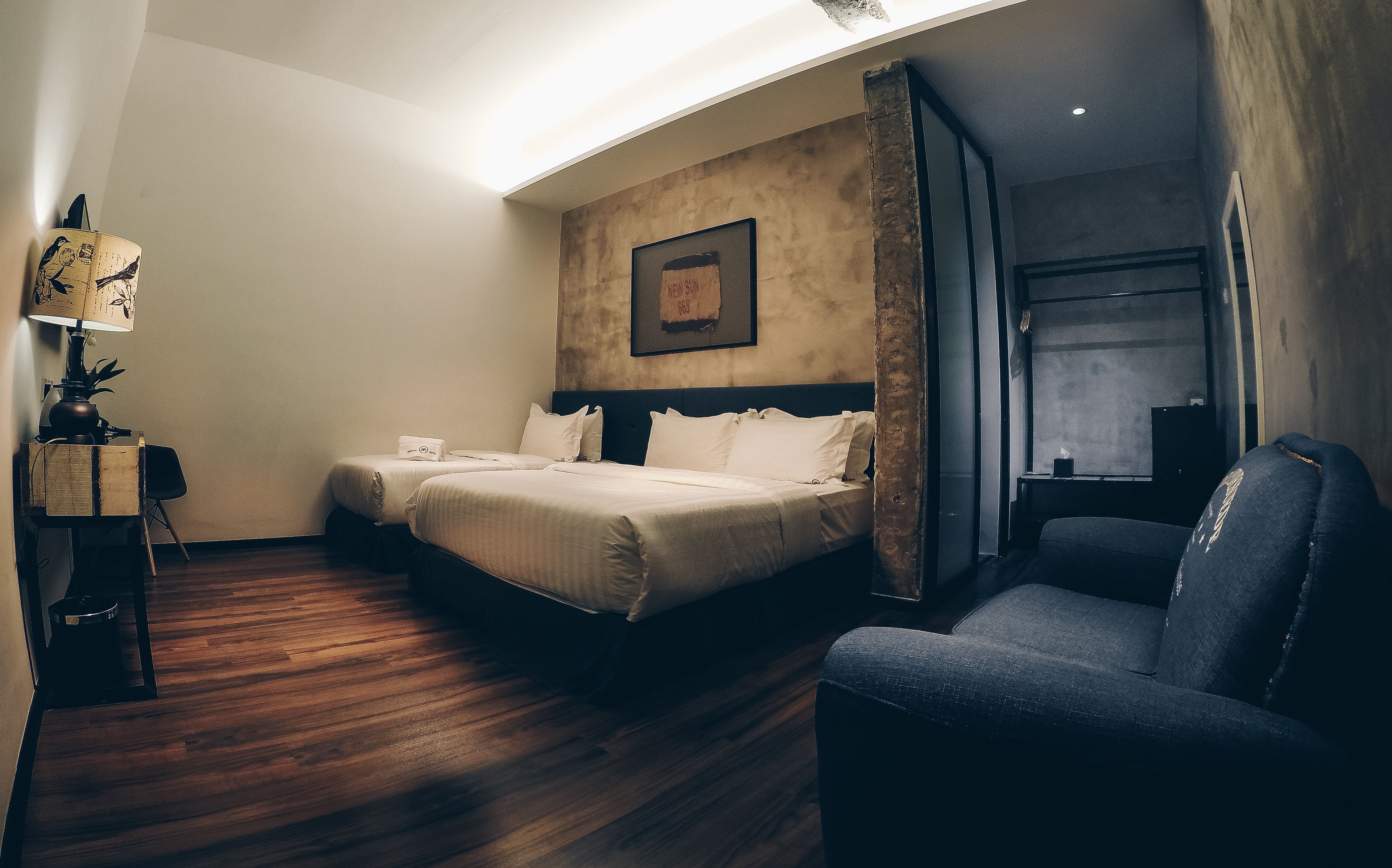 A hotel room with two beds, a desk with a lamp, a chair, and a large window.